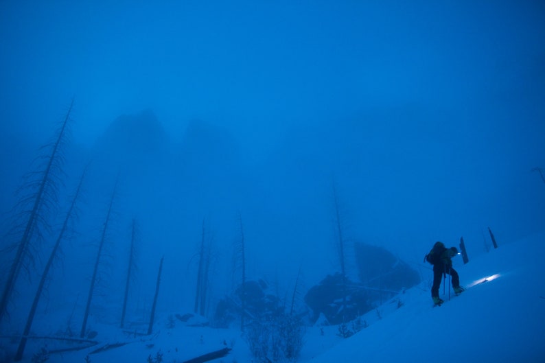 Dawn Patrol under the Spires, Montana. A backcountry skier skins up beneath granite spires in the Montana wilderness.